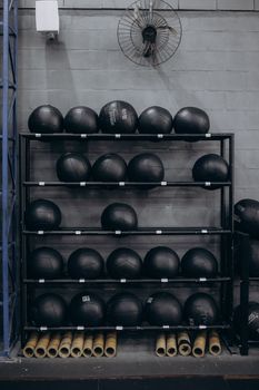 Neatly arranged medicine balls on a rack in an urban indoor gym setting.