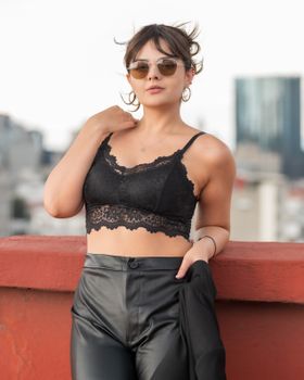 Stylish young woman in black lace top and leather pants on a rooftop. Urban summer fashion in Mexico City.