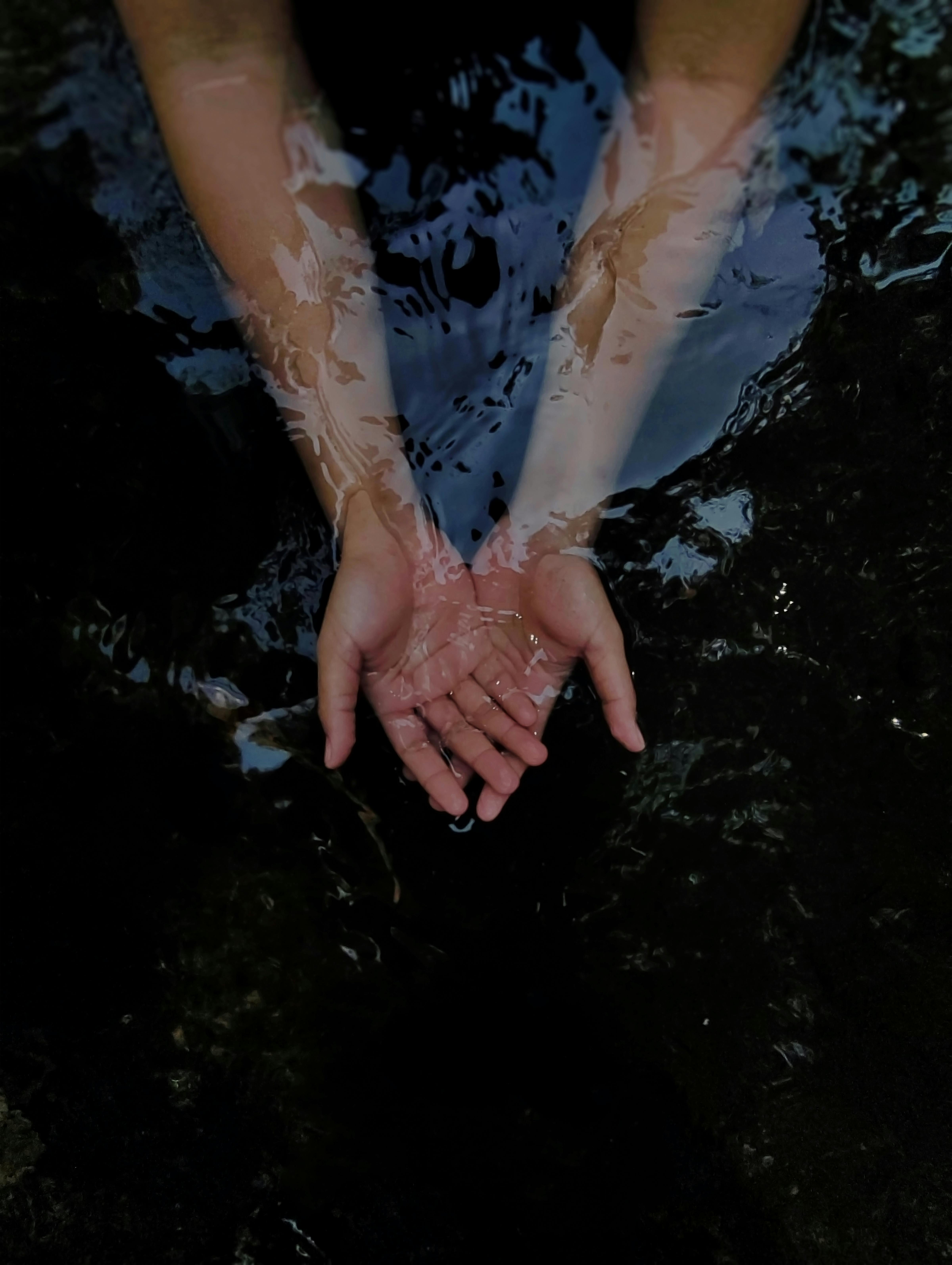 Hands reaching out in dark water, creating a moody reflection effect.