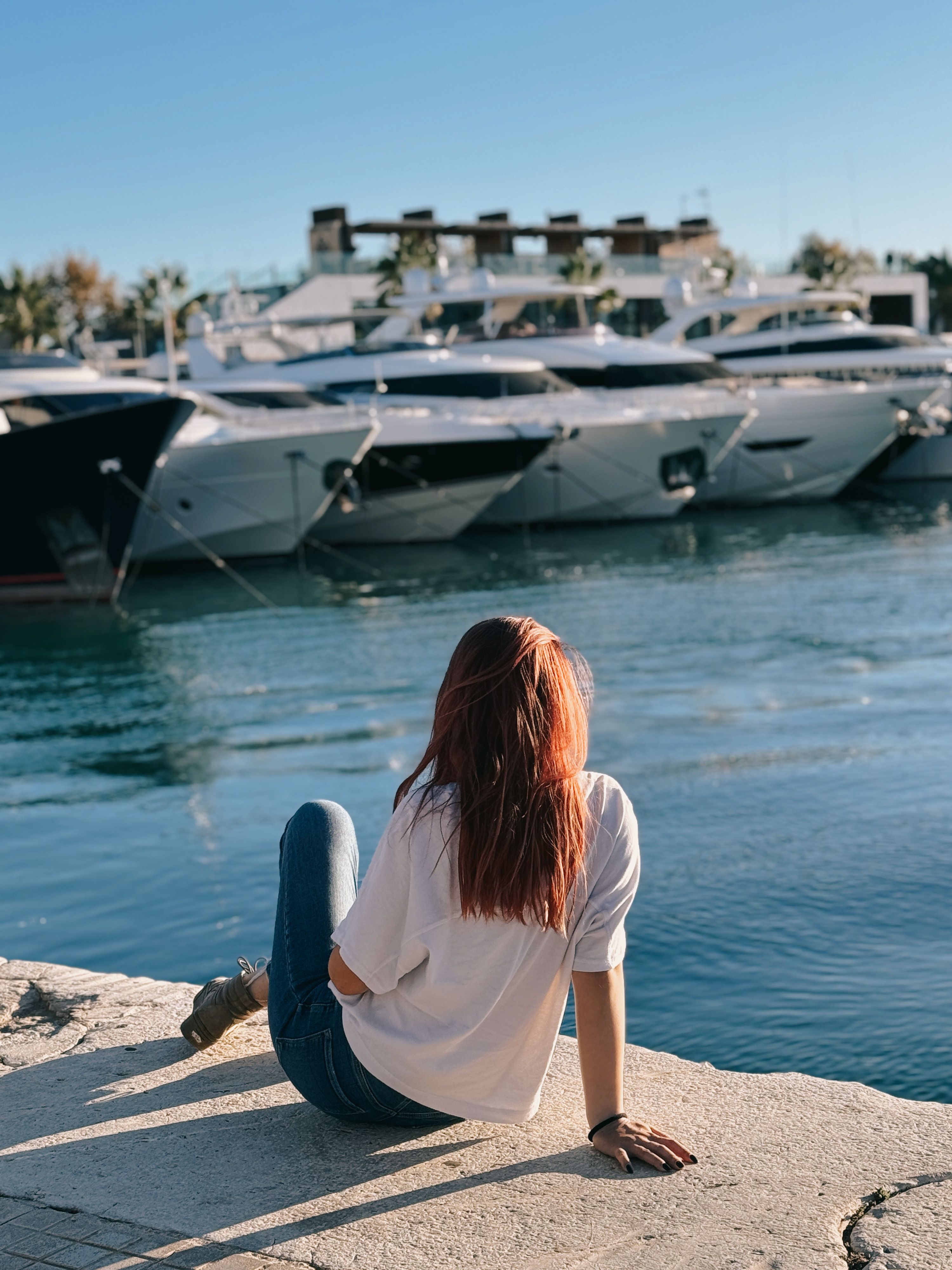 A woman sitting on the edge of a dock looking at boats · Free Stock Photo