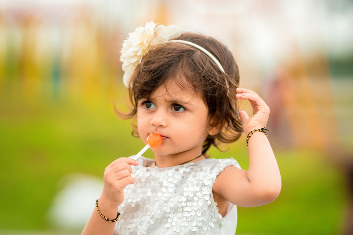Cute child with a lollipop wearing a sequin dress outdoors, embodying innocence and joy.
