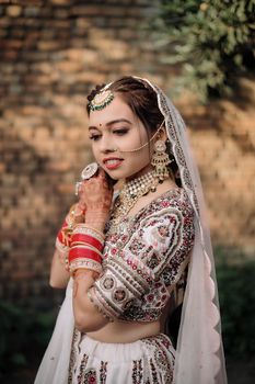 Beautiful South Asian bride in traditional attire with intricate jewelry and mehndi outdoors.
