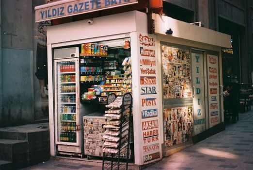 Street view of a urban newsstand selling magazines, drinks, and snacks.