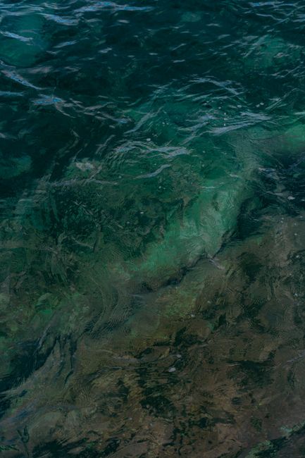 A stunning view of clear turquoise water with visible rocky ocean floor, creating abstract patterns.