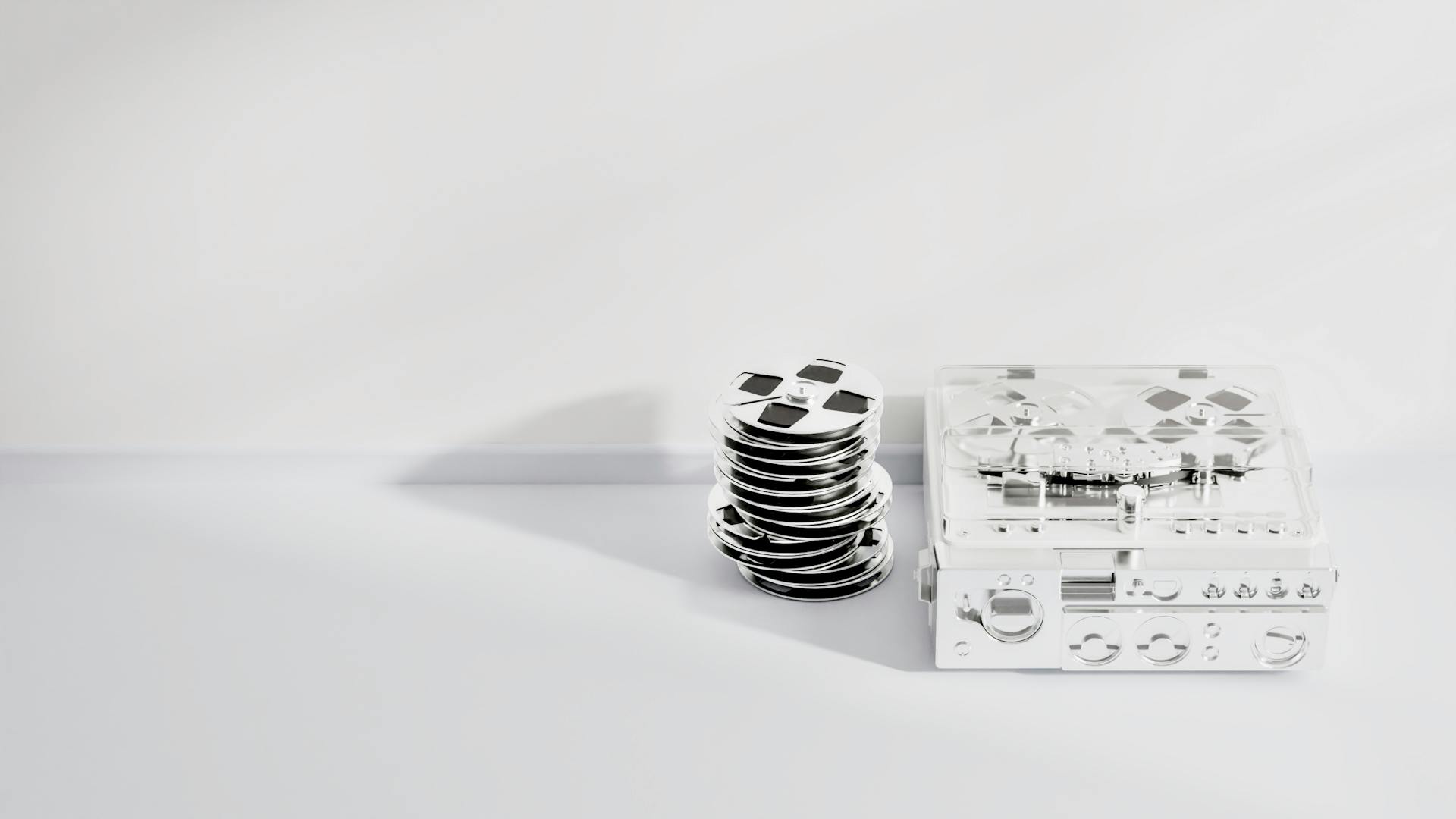 A minimalistic image of stacked reels and a clear tape recorder on a white background.