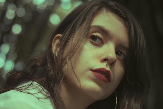 A captivating artistic portrait of a young woman with piercing eyes, set against a blurred natural background.