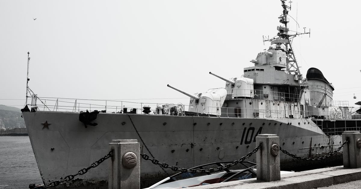 A large naval destroyer ship docked at a harbor under a gray sky.