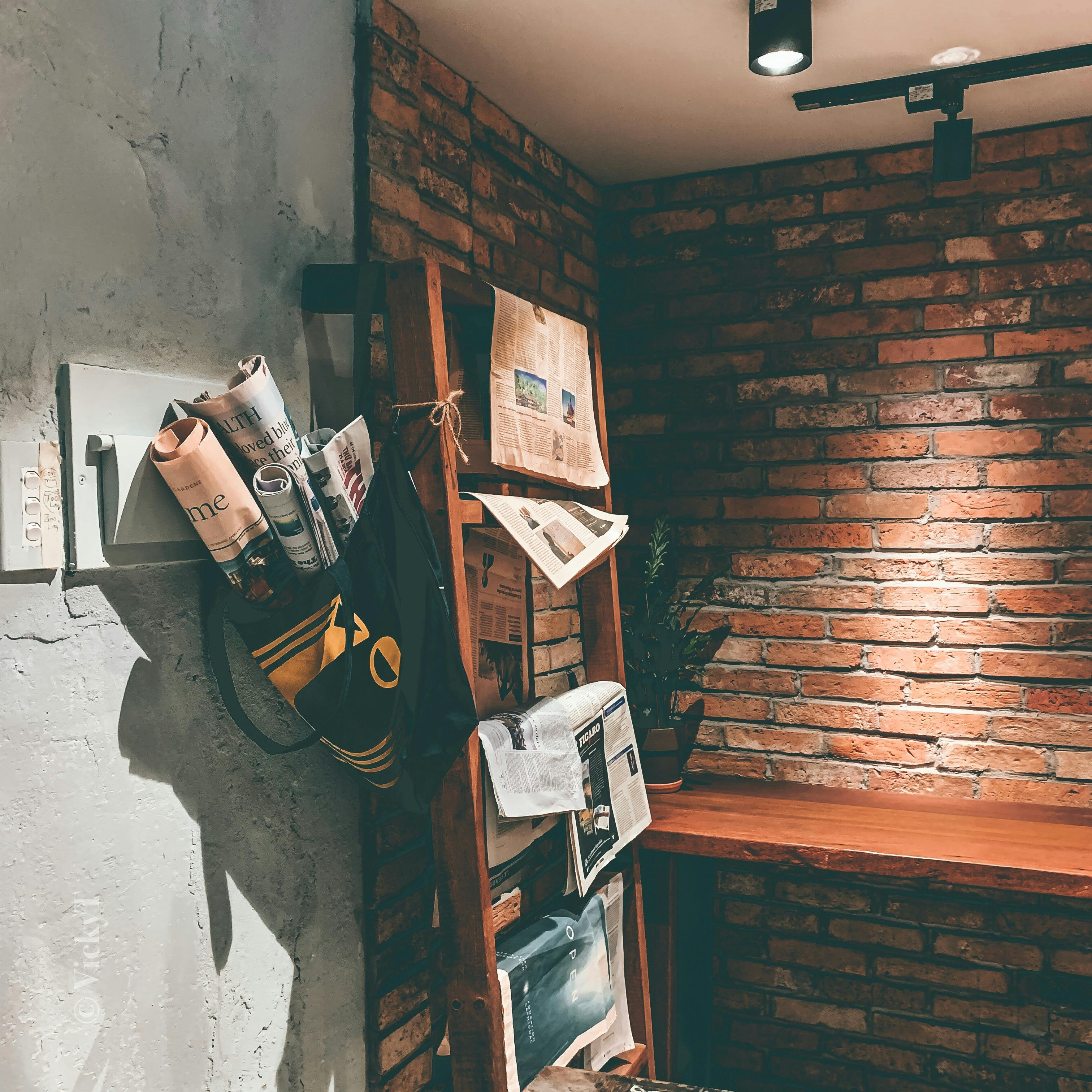 Free Brick wall interior featuring a rustic newspaper stand with various publications arranged neatly. Stock Photo