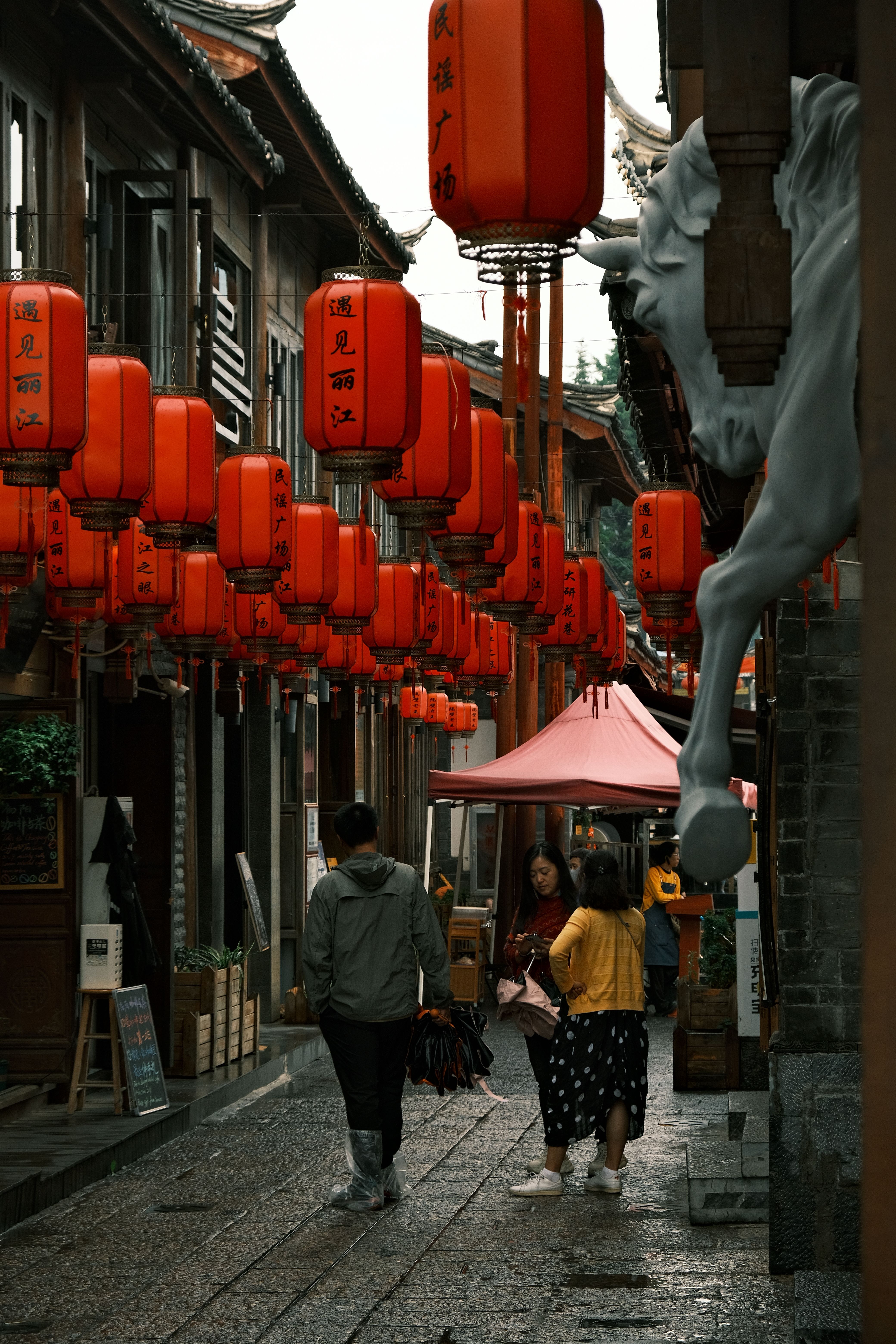 People walking down a narrow alleyway with red lanterns hanging from ...