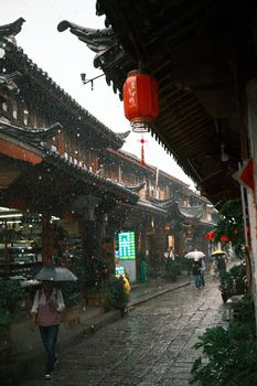Traditional Asian street scene in the rain with people under umbrellas. Cultural architecture.