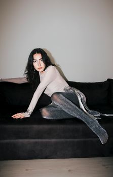 Stylish woman with black hair in elegant attire relaxing on a black sofa indoors.