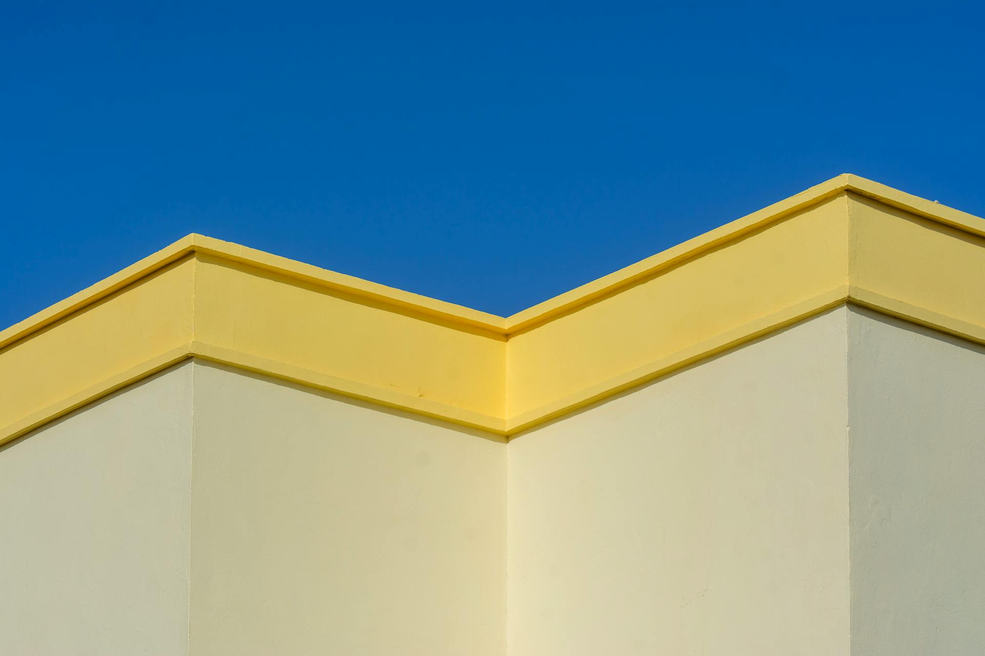 A minimalist architectural shot showcasing a modern building with a yellow roof against a clear blue sky.