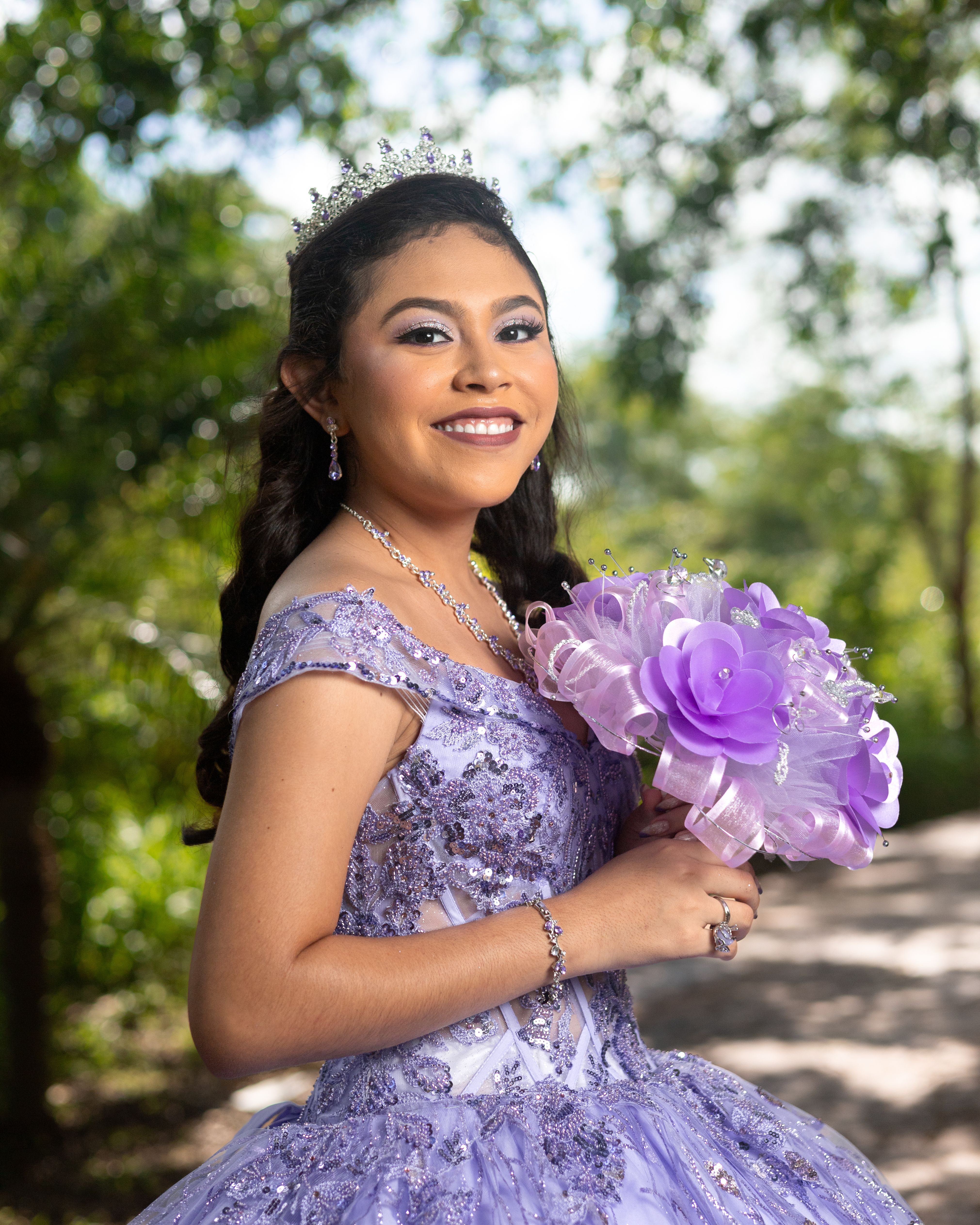 A beautiful quinceañera portrait with a purple dress and bouquet in an outdoor setting.