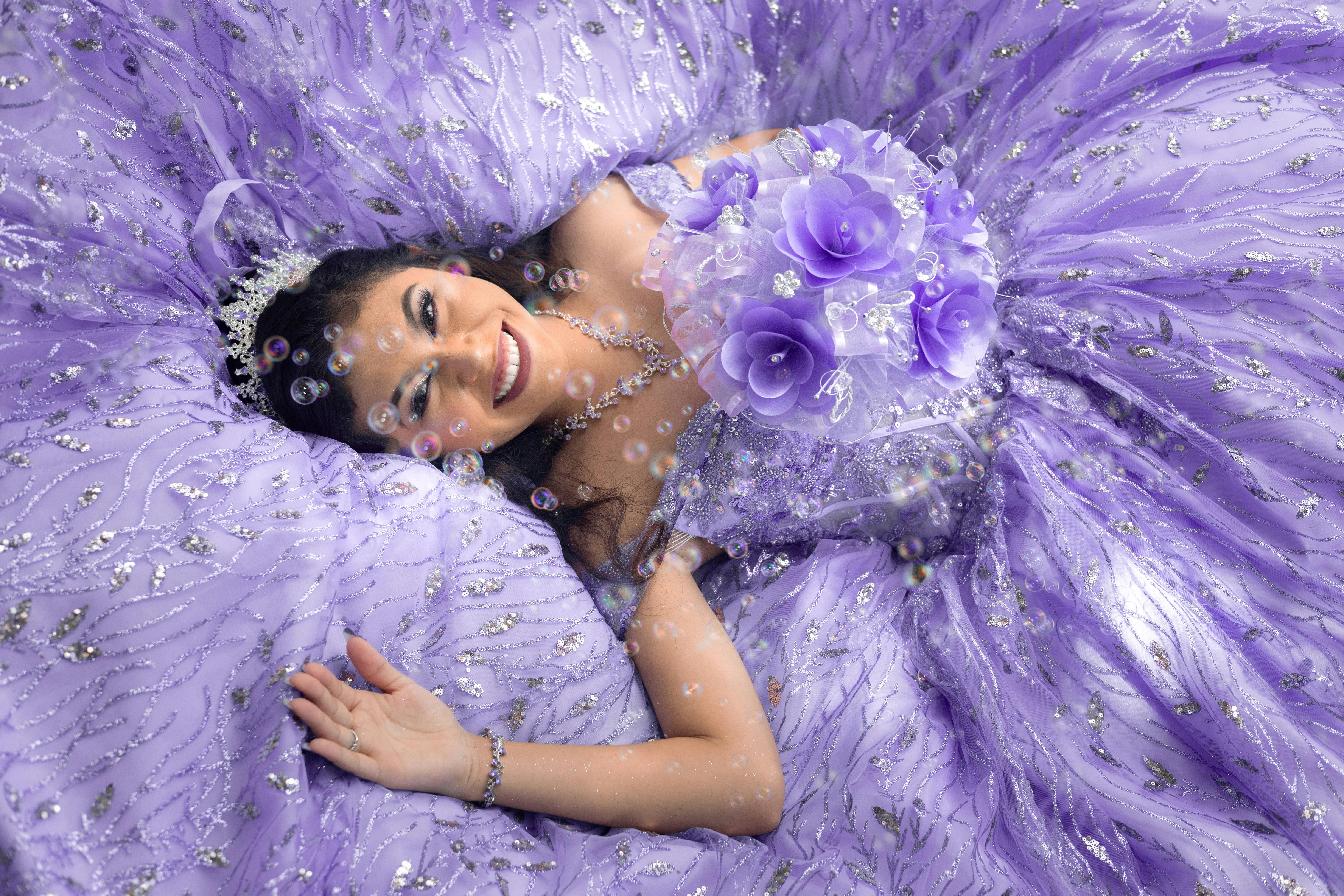 Elegant portrait of a girl in a purple quinceañera dress with tiara, in an outdoor summer setting.