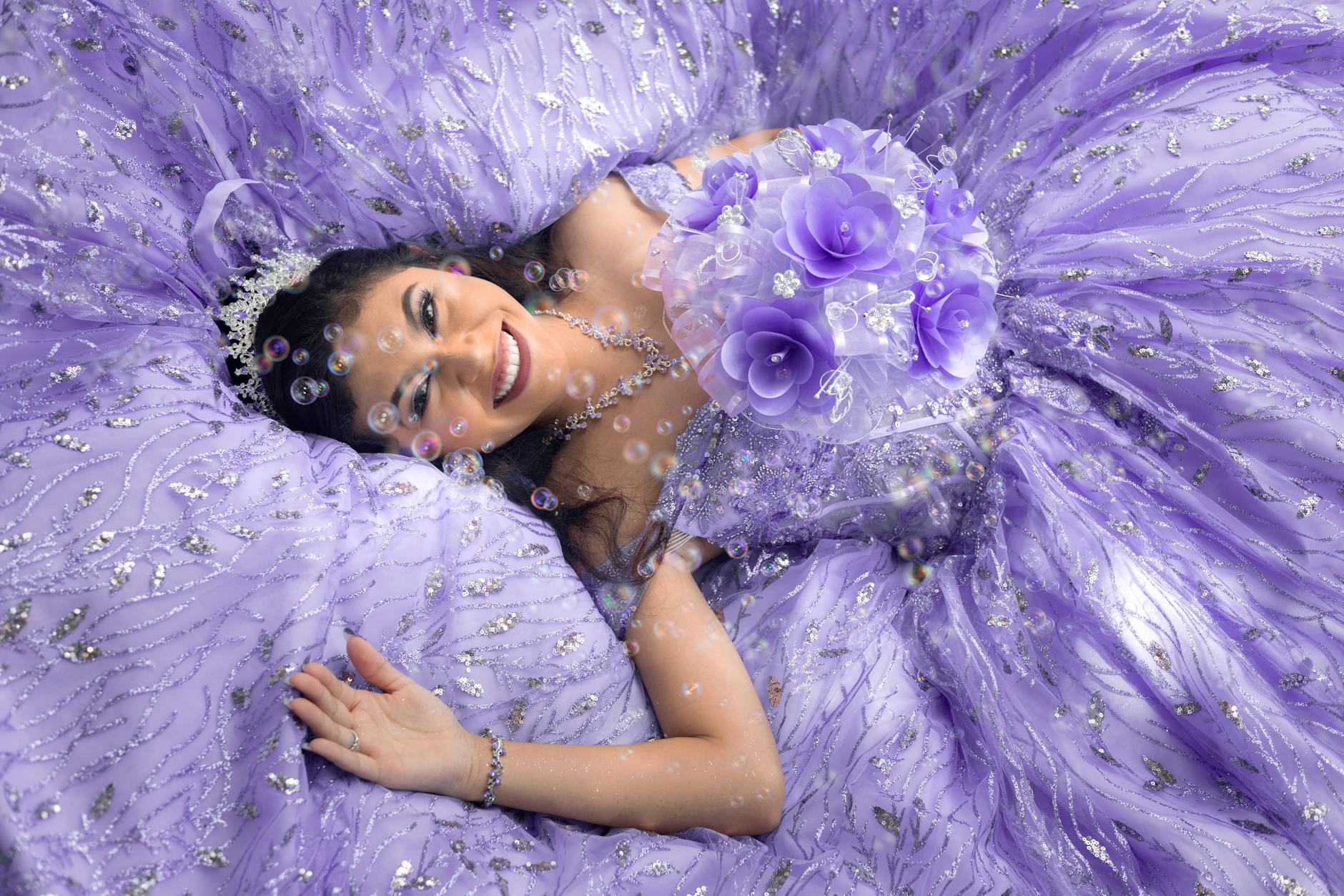 Elegant portrait of a girl in a purple quinceañera dress with tiara, in an outdoor summer setting.