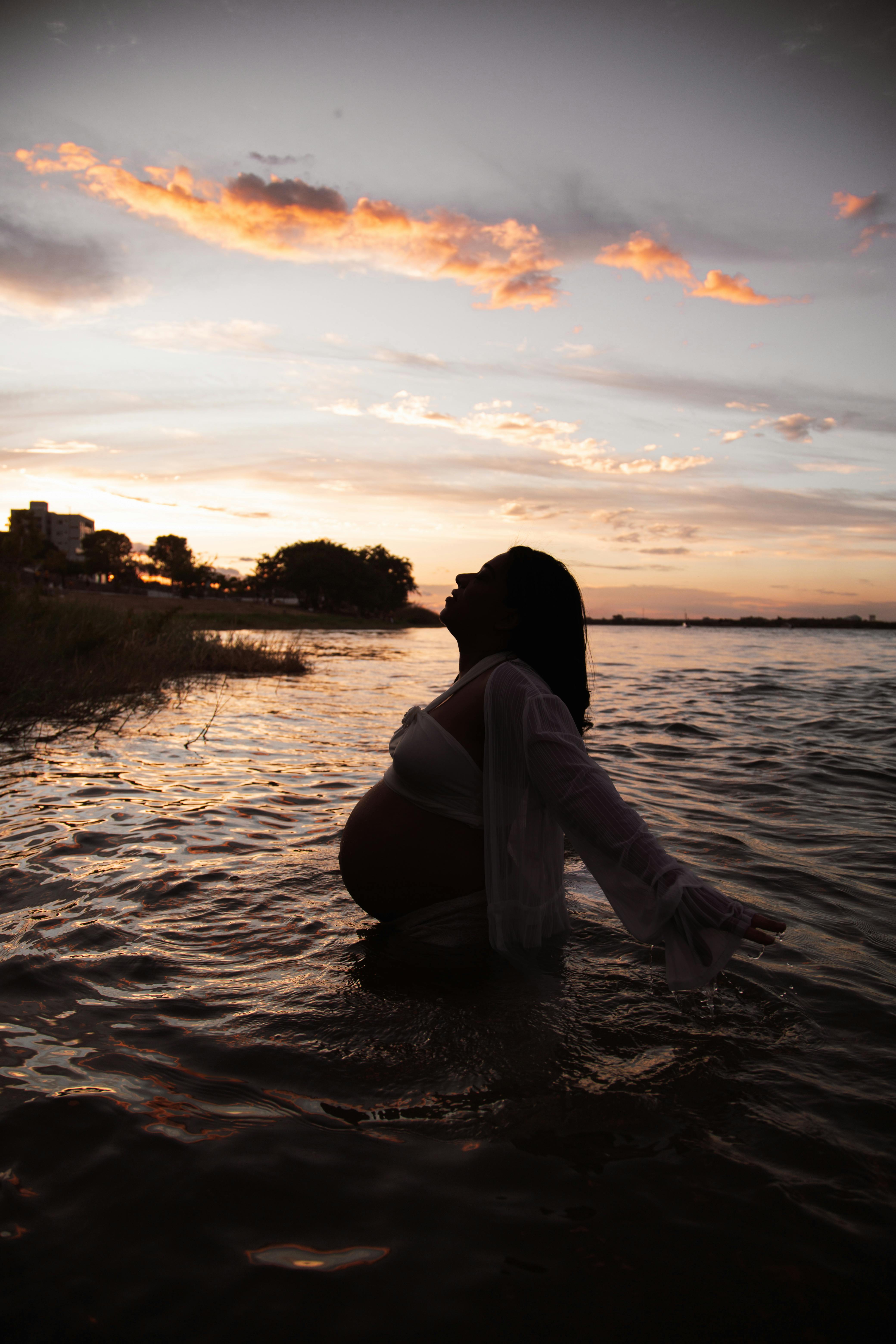 a pregnant woman standing in the water at sunset