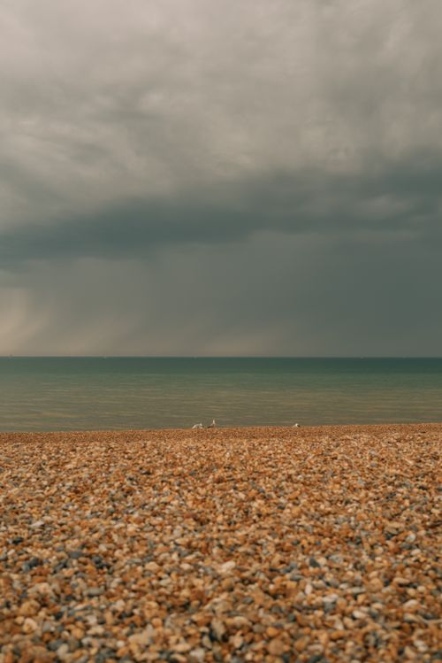 Free Pebble beach with stormy sky and calm sea, creating a dramatic coastal scene. Stock Photo