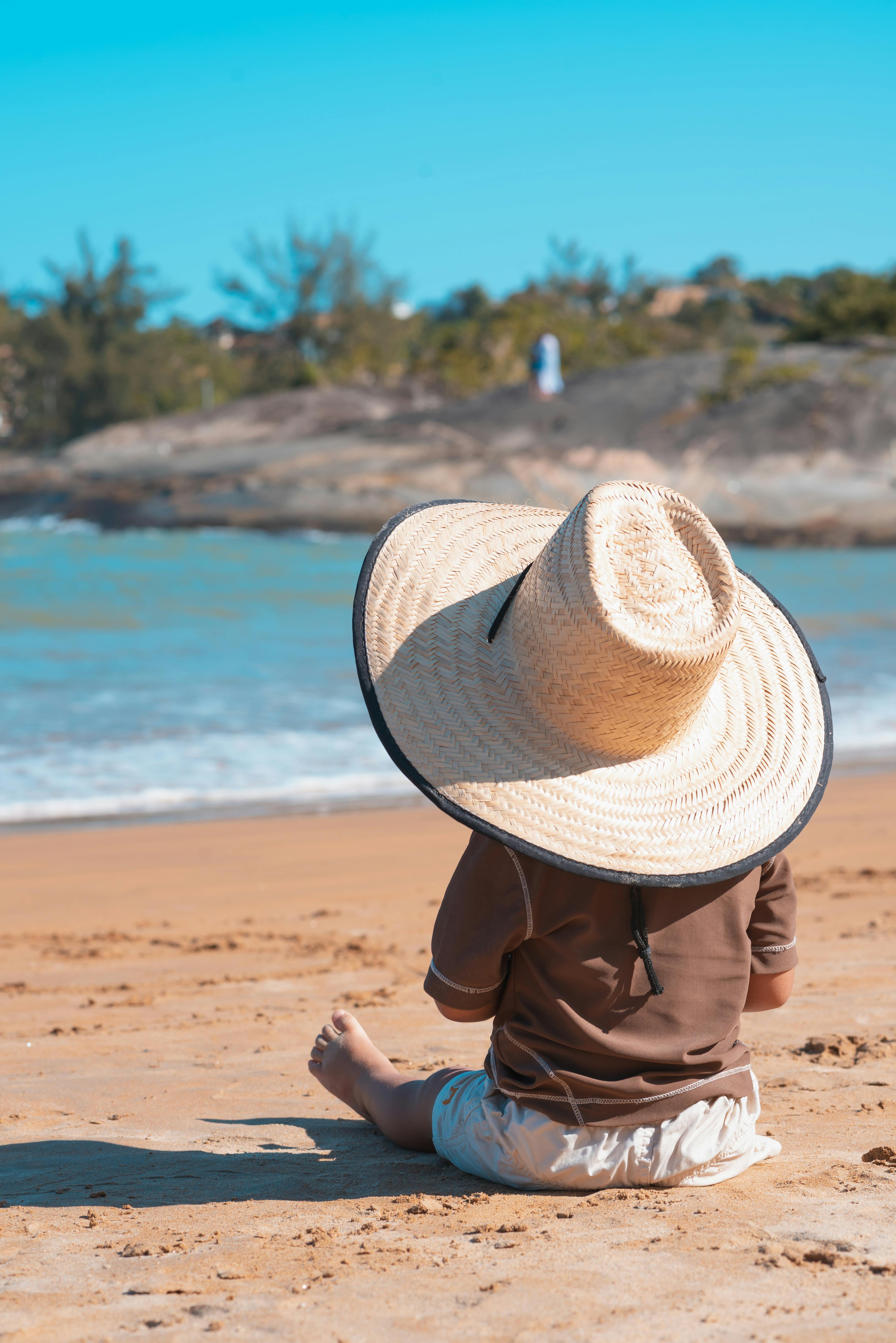 back view of a child wearing a sunhat sitting on the beach