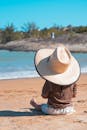 一个戴着大遮阳帽的小孩坐在海边的沙滩上