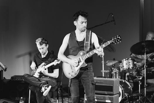 Black and white image capturing a live music band performance with guitar and drum solo.