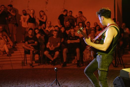 A guitarist plays passionately on stage during an outdoor concert, engaging a diverse audience.