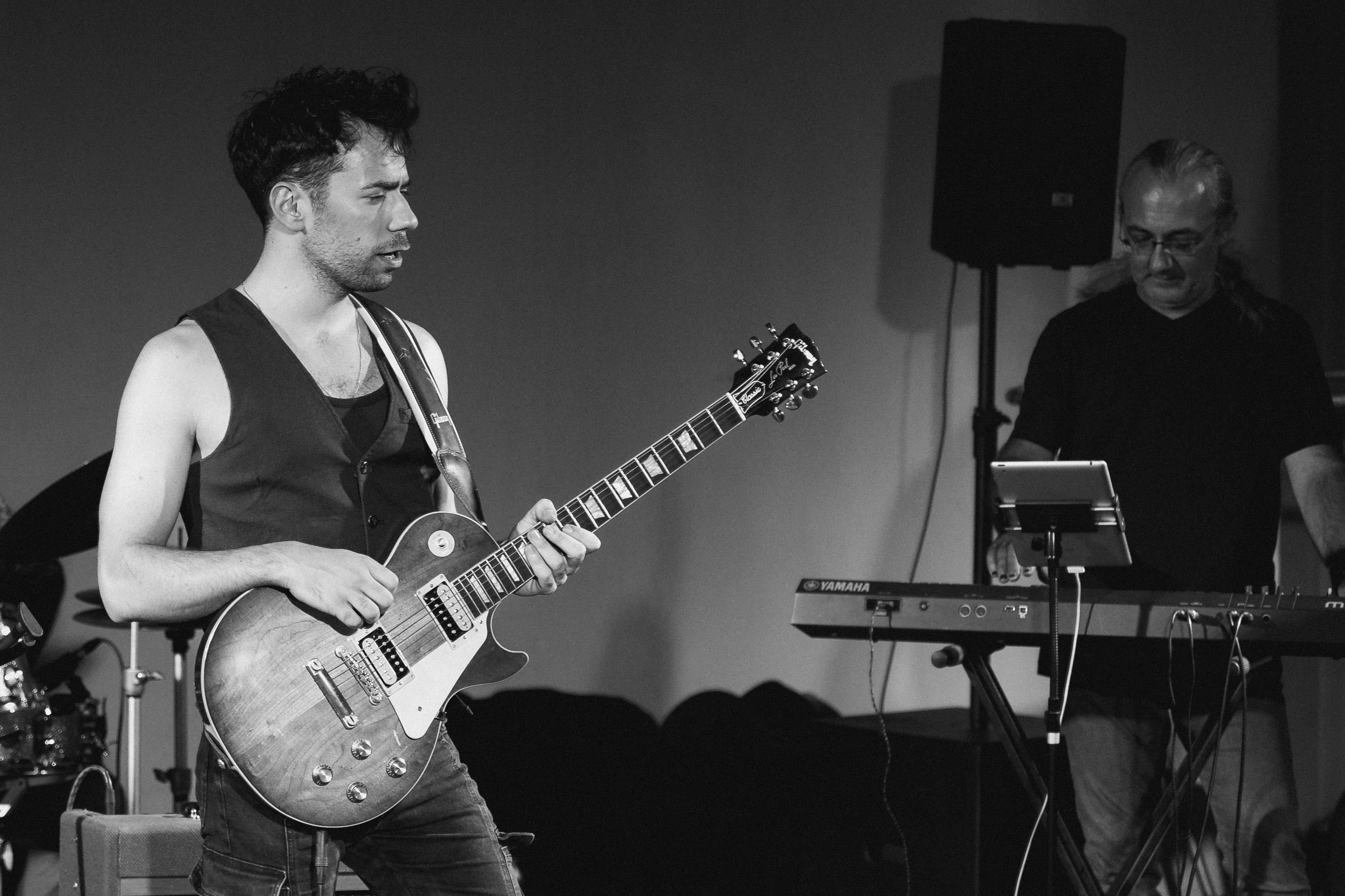 Black and white image of musicians playing guitar and keyboard on stage during a live performance.