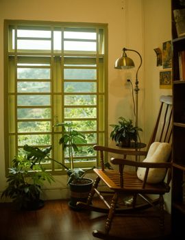 Warm and inviting home interior featuring a wooden rocking chair, window view, and lush houseplants.