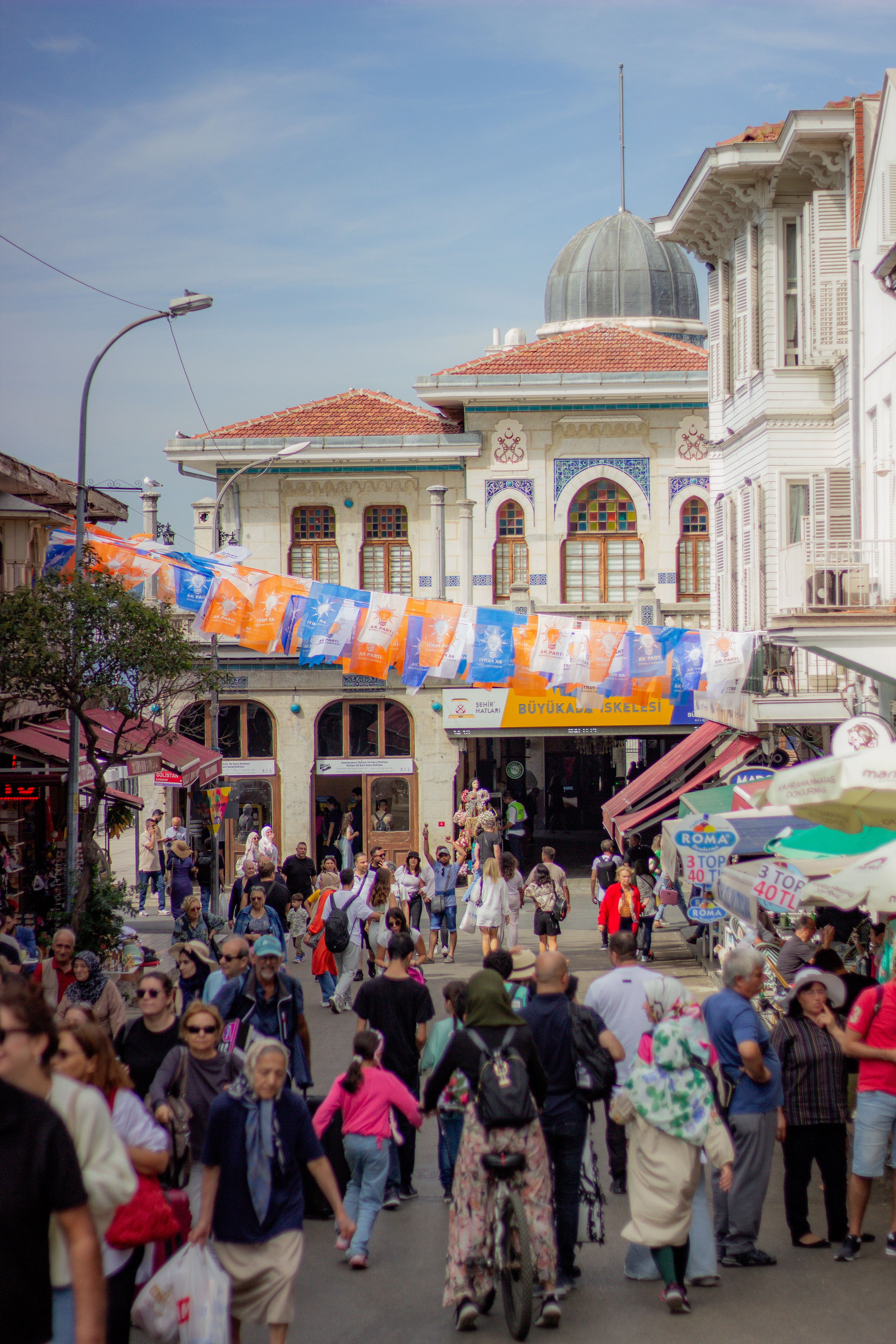 Lively crowd in a historic street market featuring diverse architecture and vibrant atmosphere under daylight.