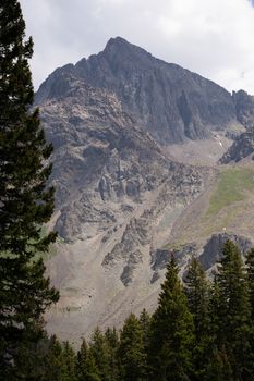 A breathtaking view of a rugged mountain peak surrounded by evergreen trees under a clear sky.