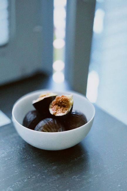 Close-up of fresh figs in a white bowl by a window with natural daylight.