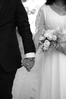 A stylish black and white photo of a bride and groom holding hands. The bride is holding a bouquet.