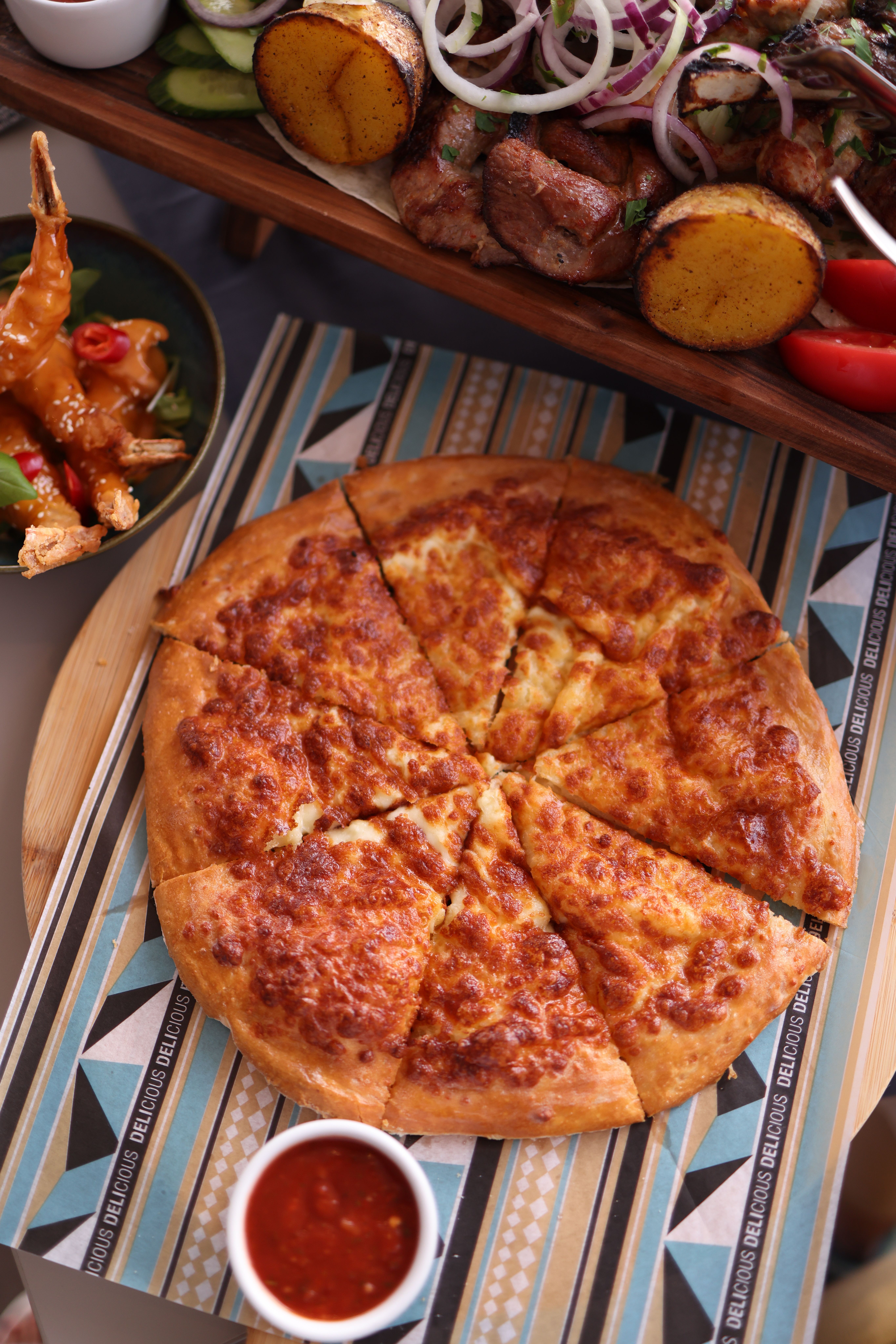 A delicious cheesy pizza served with various side dishes and a dipping sauce.