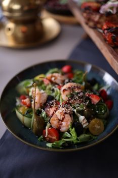 A vibrant prawn salad featuring cherry tomatoes and caper berries, surrounded by fresh greens.