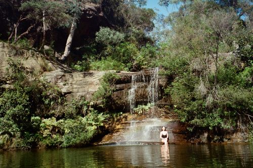 Free A tranquil scene of a waterfall surrounded by lush greenery with a person in the water. Stock Photo