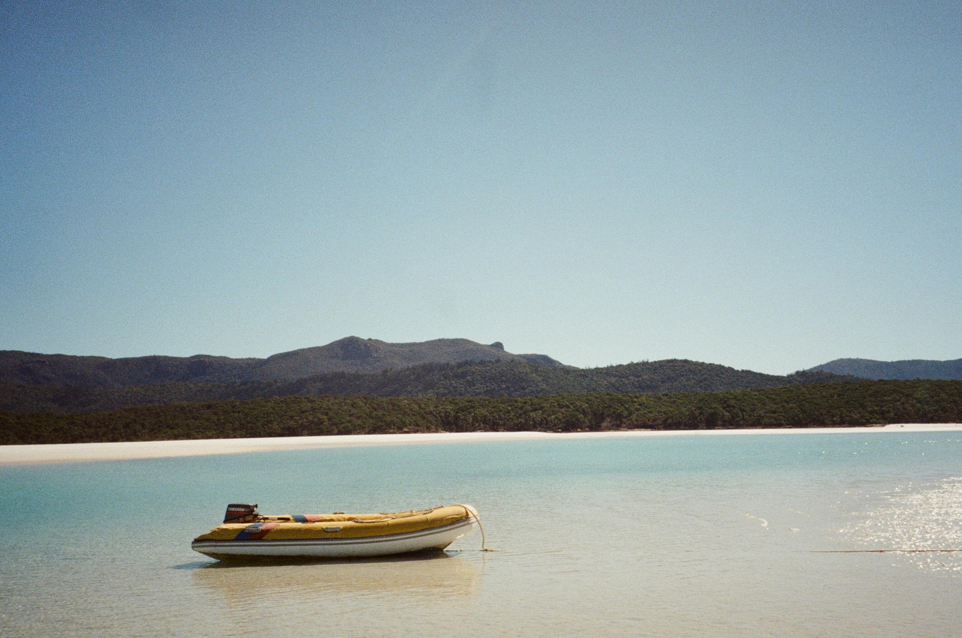 Serene beach landscape featuring a yellow dinghy on calm aqua waters with a mountain backdrop.