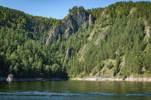 Free Stunning view of a lush forest and rocky mountain reflecting on a serene lake under a clear blue sky. Stock Photo