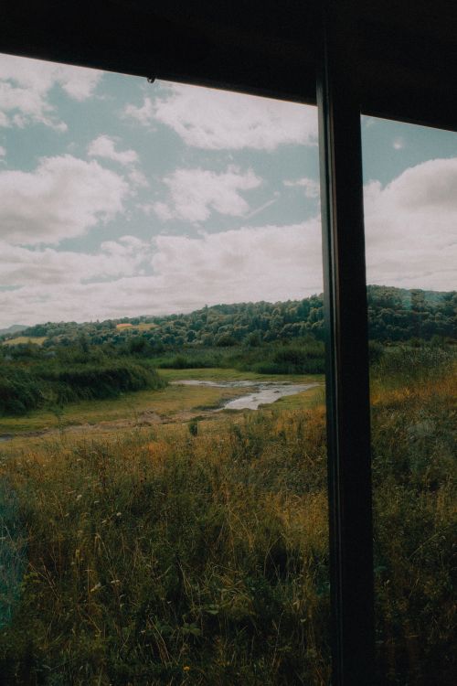 Free A serene landscape with fields, trees, and cloudy sky viewed through a window frame, evokes tranquility. Stock Photo