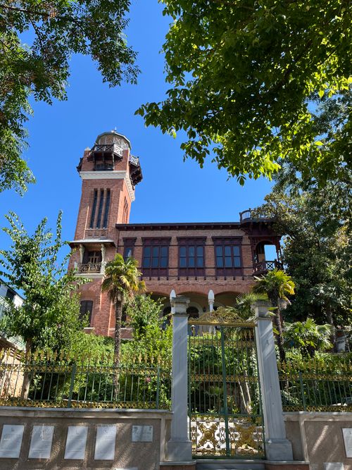 Free A historic brick building with a distinctive tower surrounded by trees and garden. Stock Photo