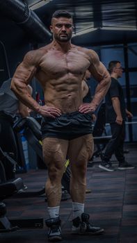 Muscular bodybuilder posing confidently indoors in a gym.