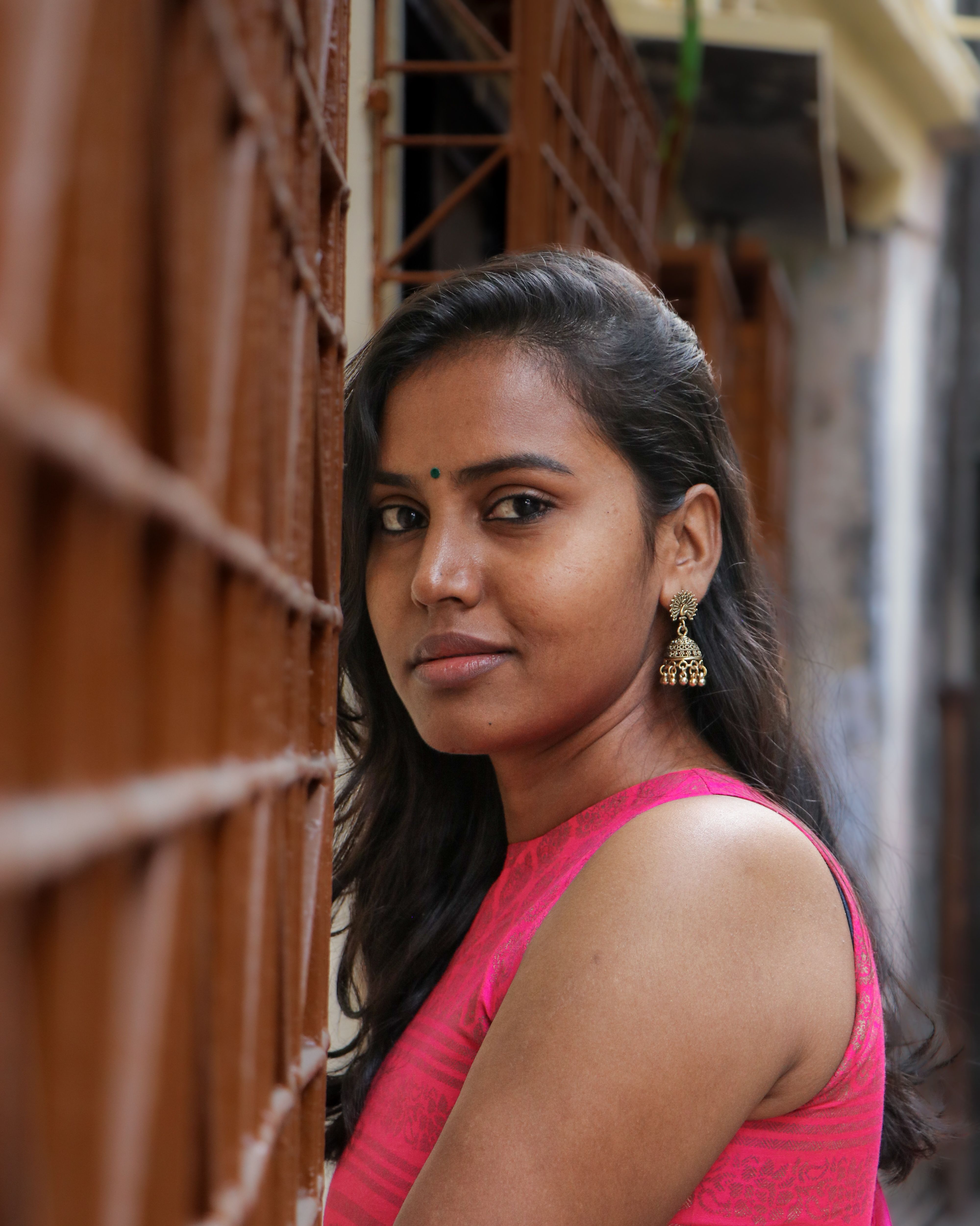 Portrait of a confident woman in pink dress posing against urban backdrop, showcasing elegance.