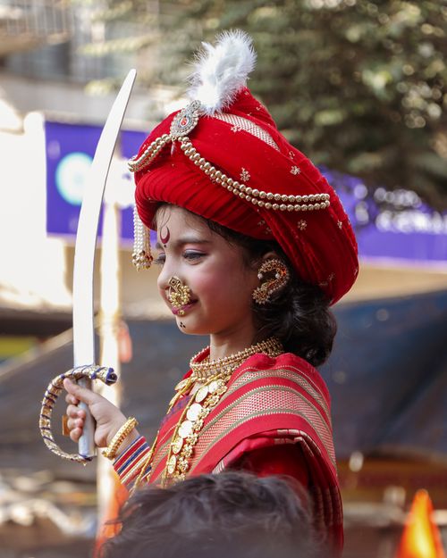 Free A child in vibrant traditional attire and jewelry holding a sword during an outdoor festival. Stock Photo