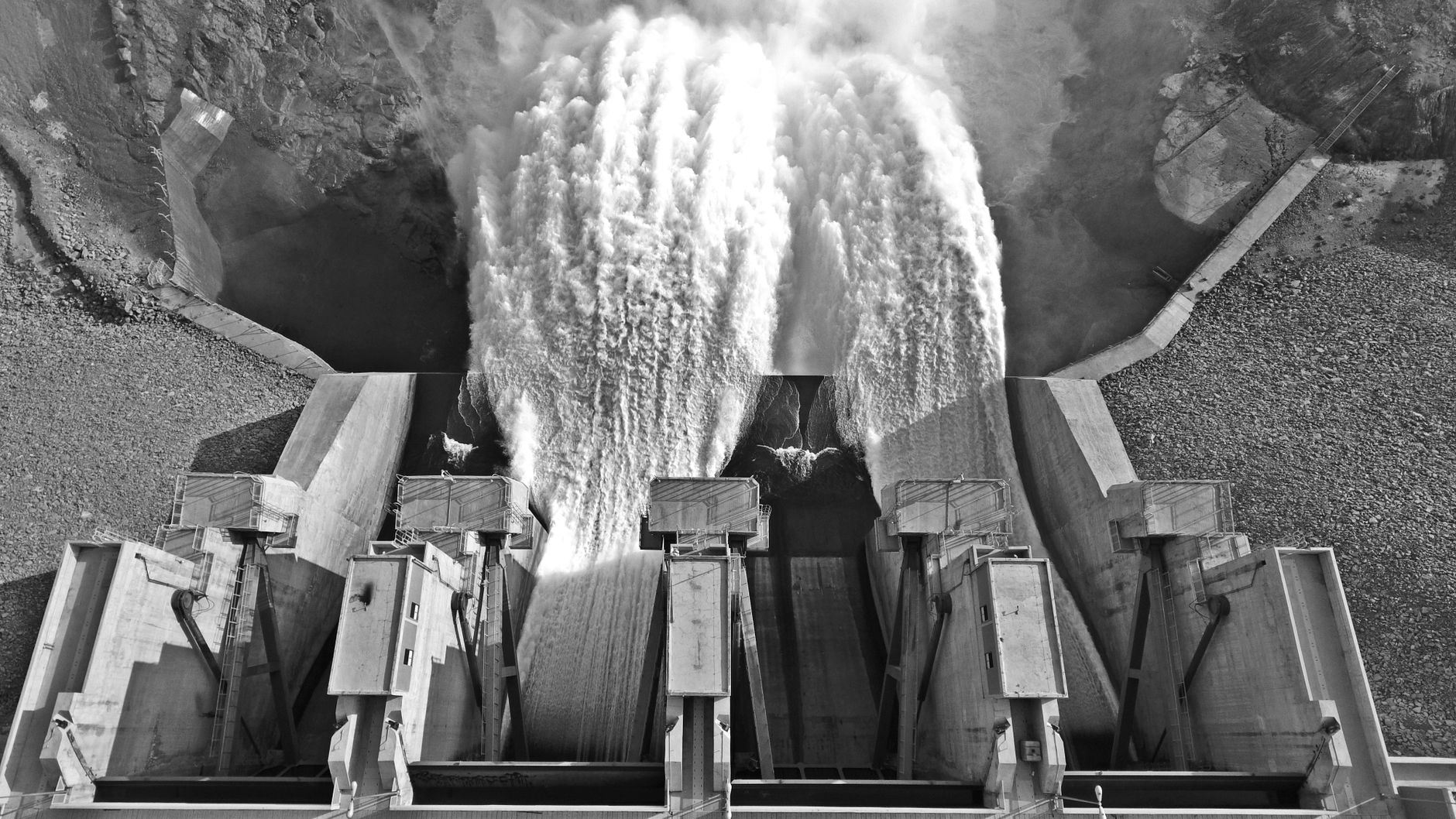 Monochrome aerial view of a dam releasing water, showcasing engineering marvel.