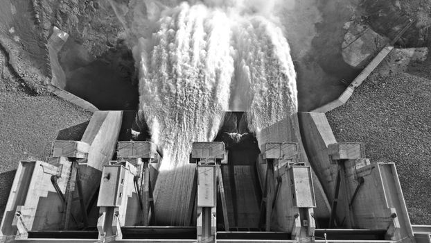 Monochrome aerial view of a dam releasing water, showcasing engineering marvel.