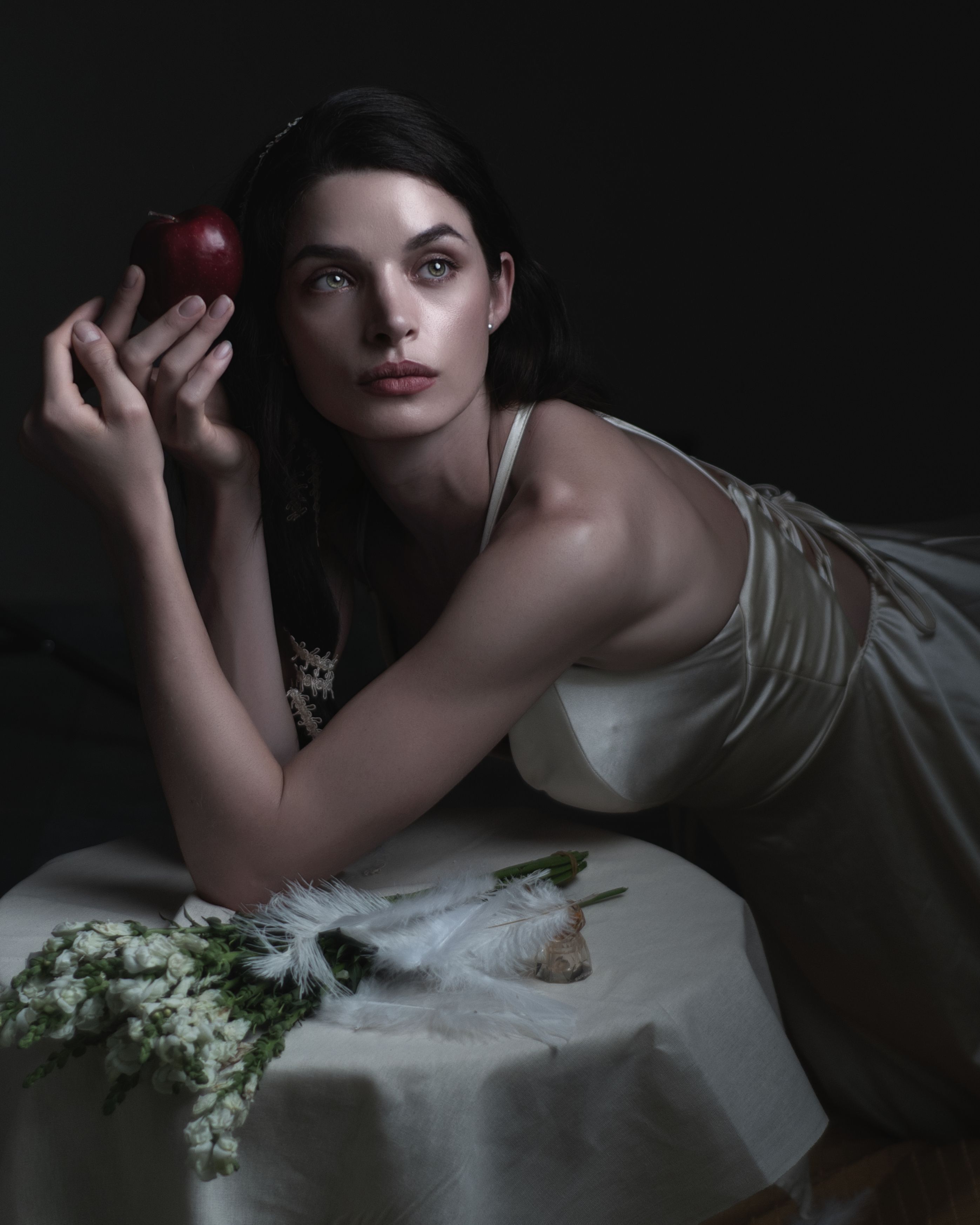 Artistic portrait of a woman holding a red apple with a dreamy expression.
