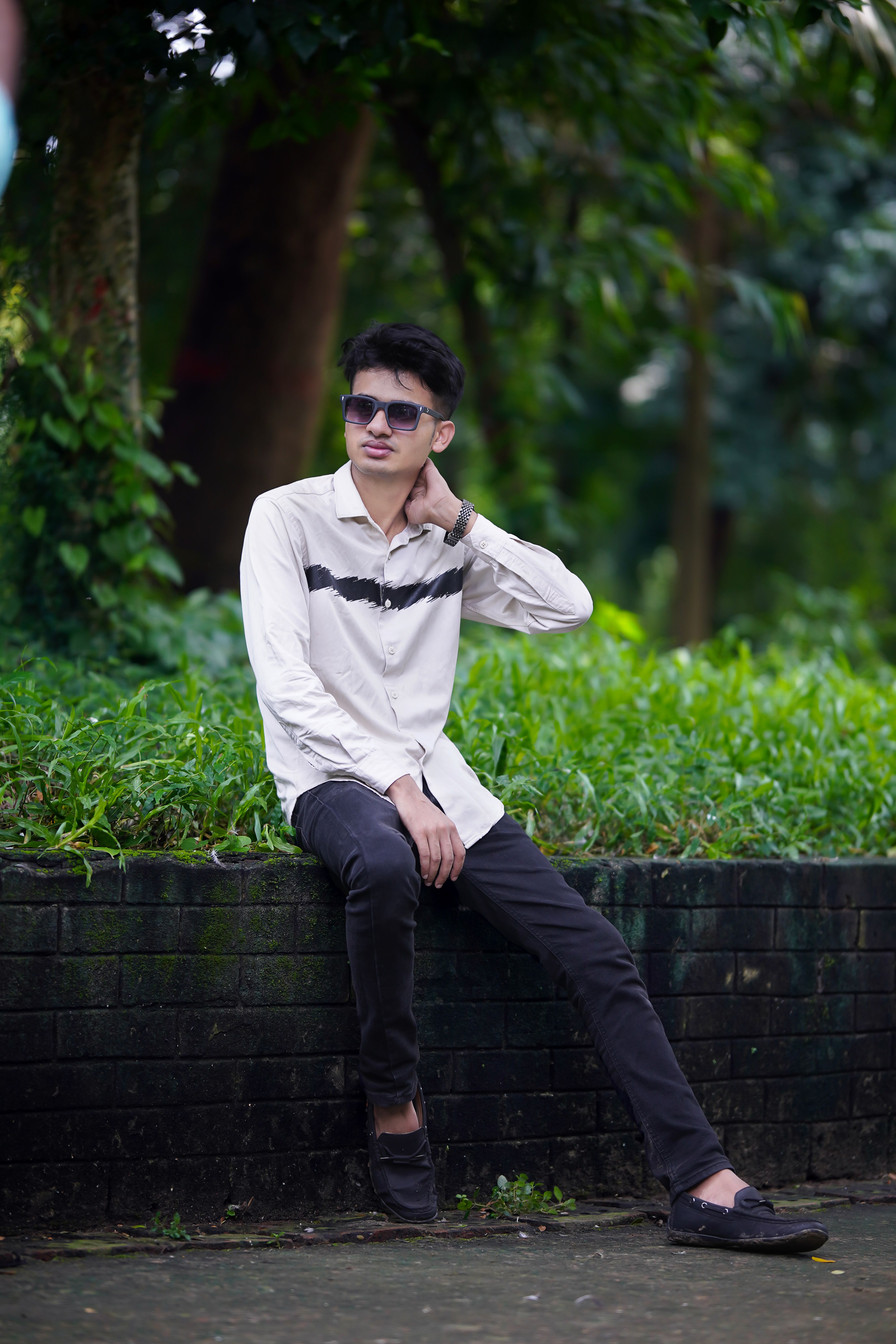 Casual portrait of a young man in sunglasses sitting outdoors in a vibrant park.