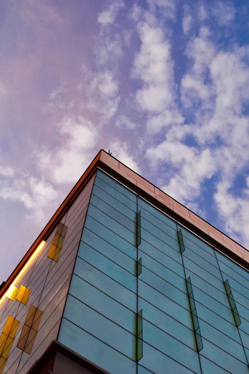 Free Contemporary glass building facade reflecting the sky with scattered clouds. Stock Photo