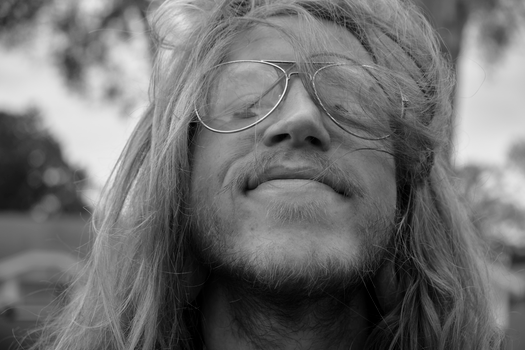 Close-up black and white portrait of a long-haired man smiling with sunglasses.