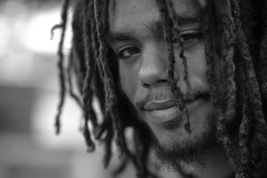 A close-up black and white portrait of an adult with dreadlocks and a subtle smile.