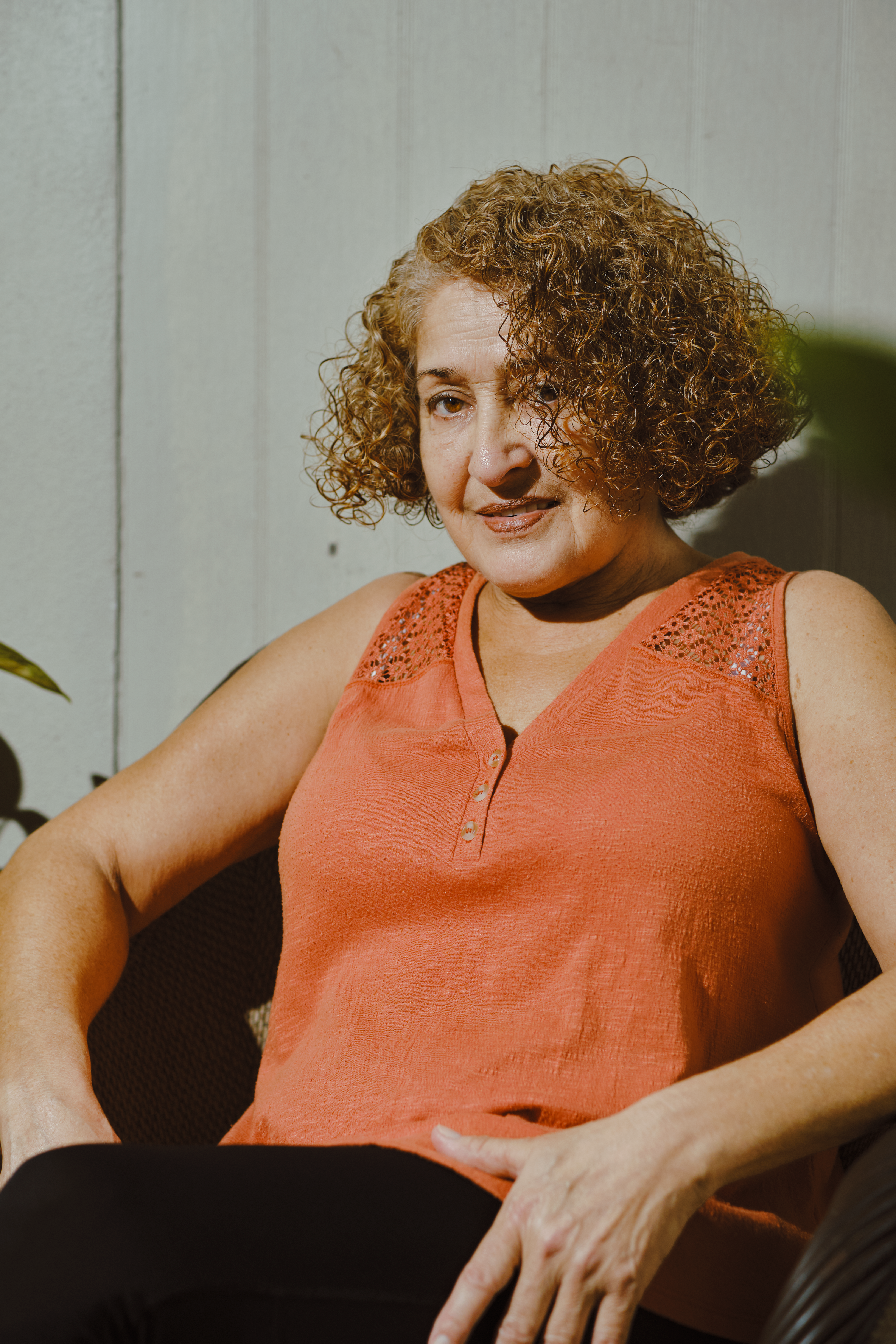 Portrait of a middle-aged woman with curly hair and a smile, seated indoors.