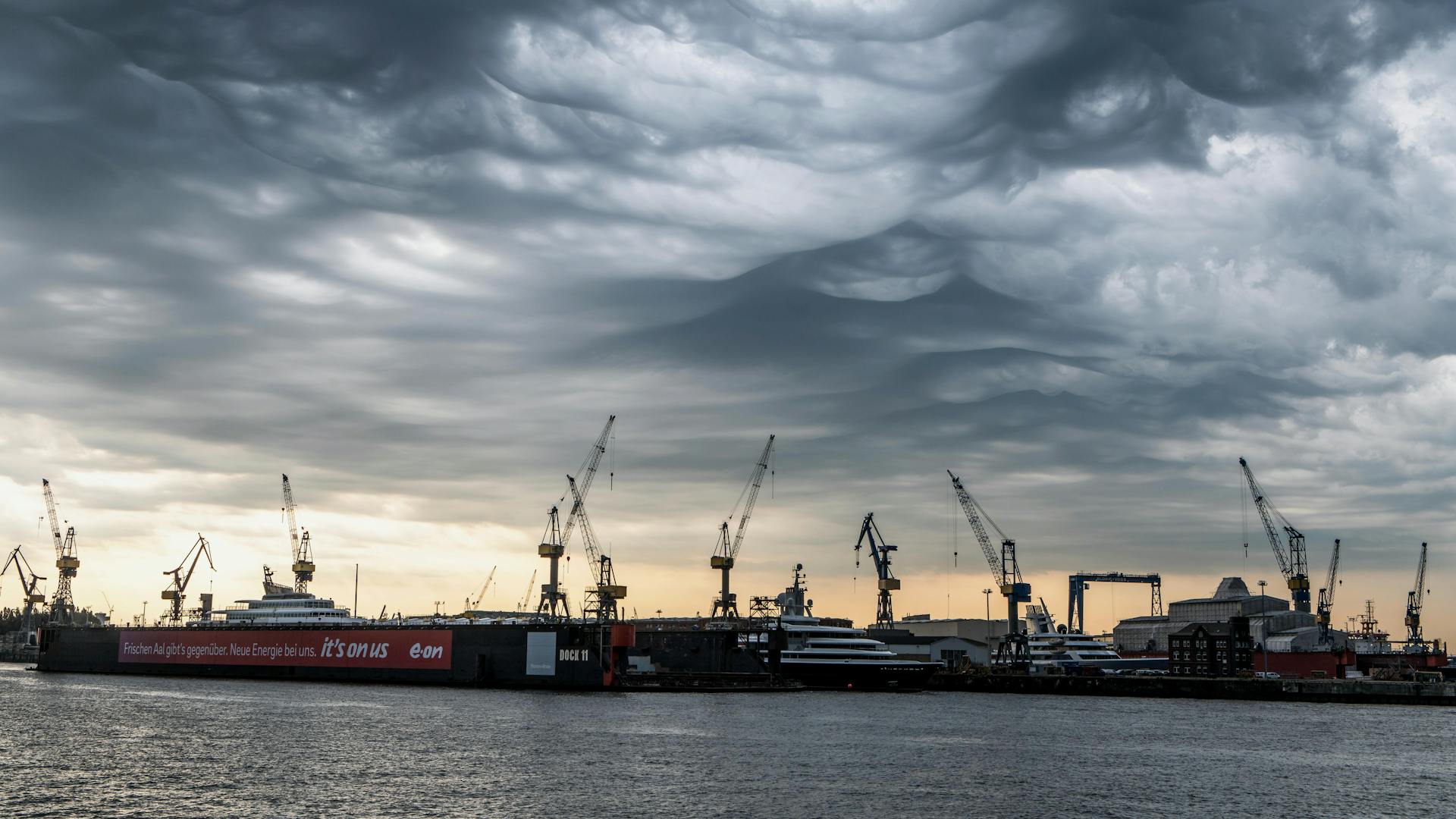 Dramatic sky over Hamburg harbor with cranes and ships during sunrise.